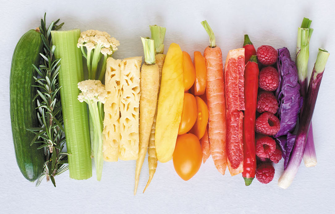Flat lay of rainbow spectrum gradient of healthy fruit and vegetables on white background